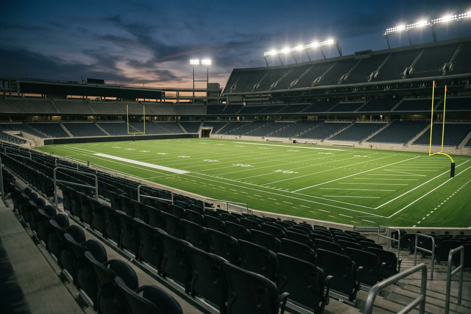 Empty stadium seats and a floodlit American football field at dusk before kickoff