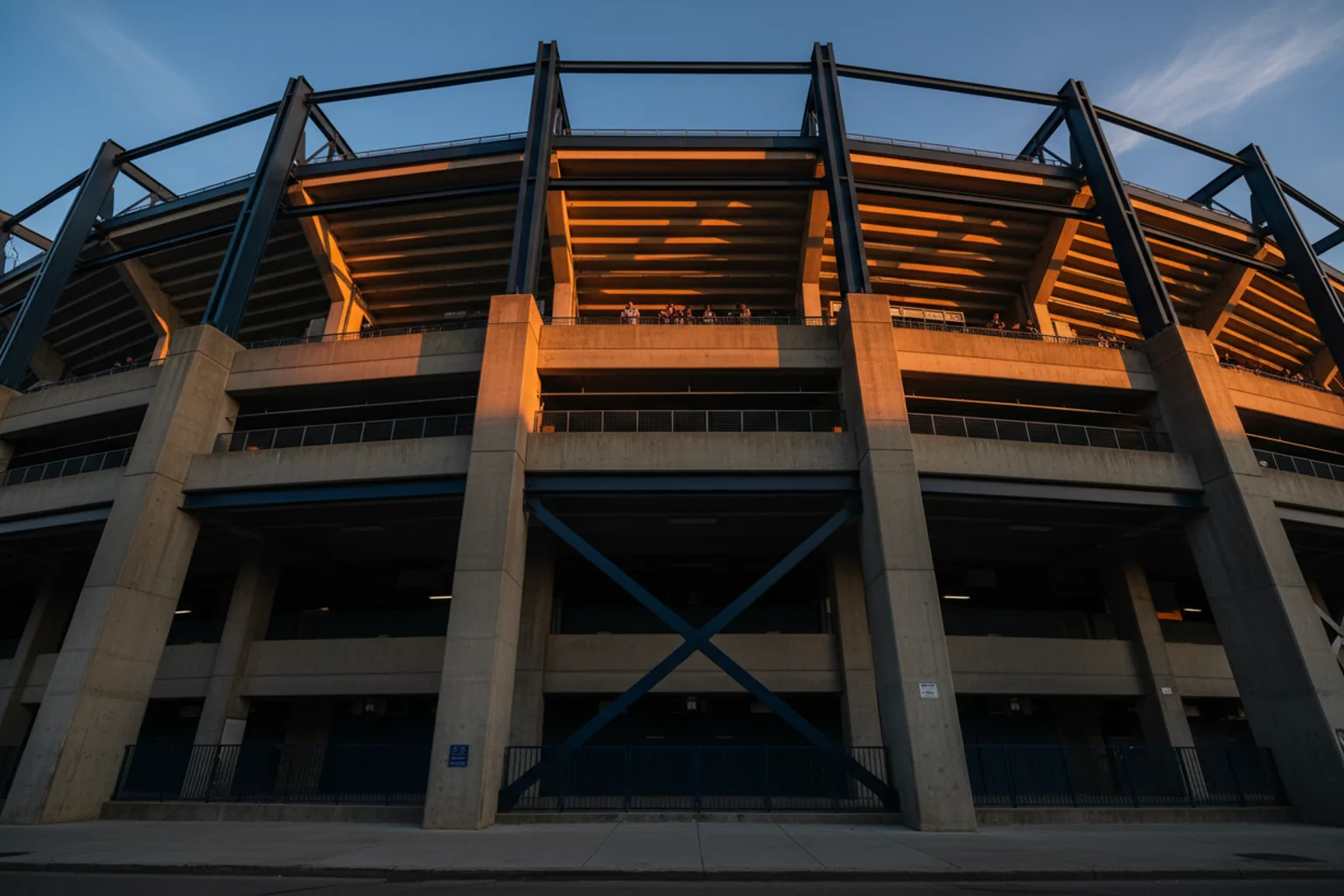 Low angle up a stadium's exterior facade lit burnt orange by the setting sun