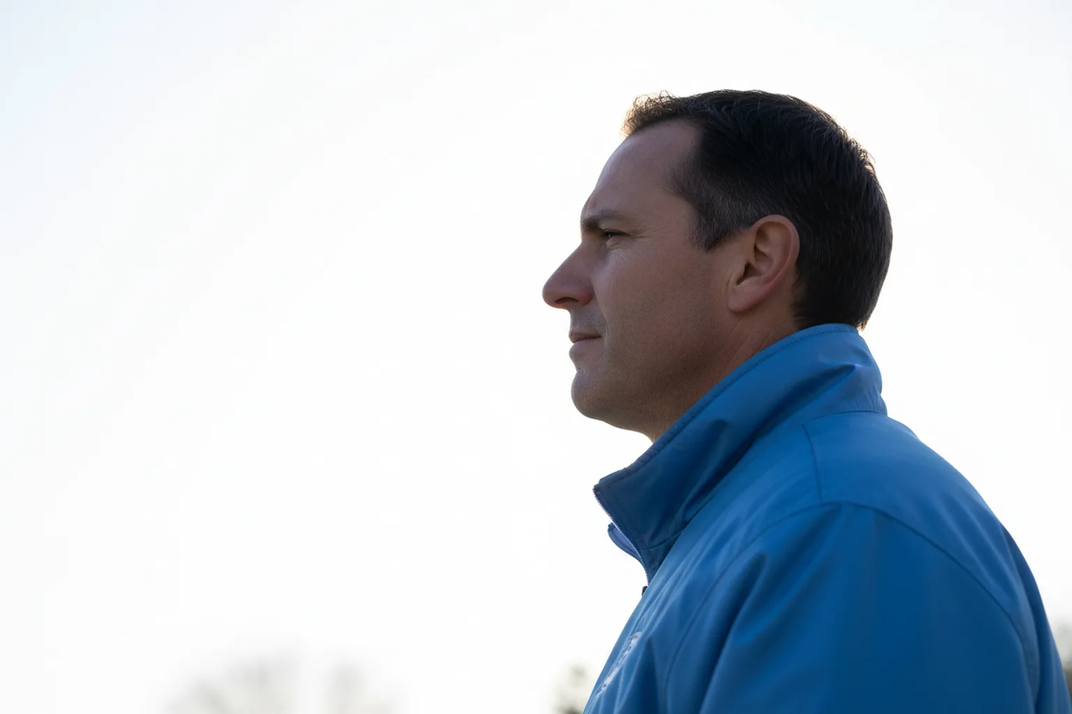 A fan in a powder blue jacket photographed in side profile against a bright, blown-out white sky