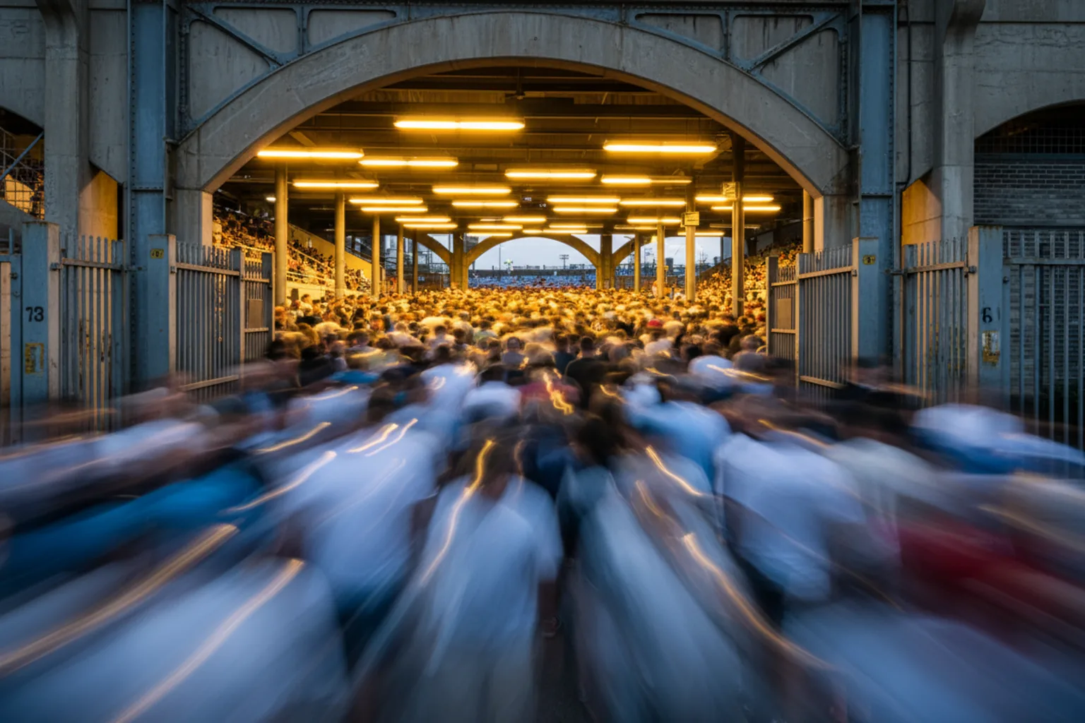 Fans blurred into streaks of powder blue and gold as they stream through a stadium gate at dusk