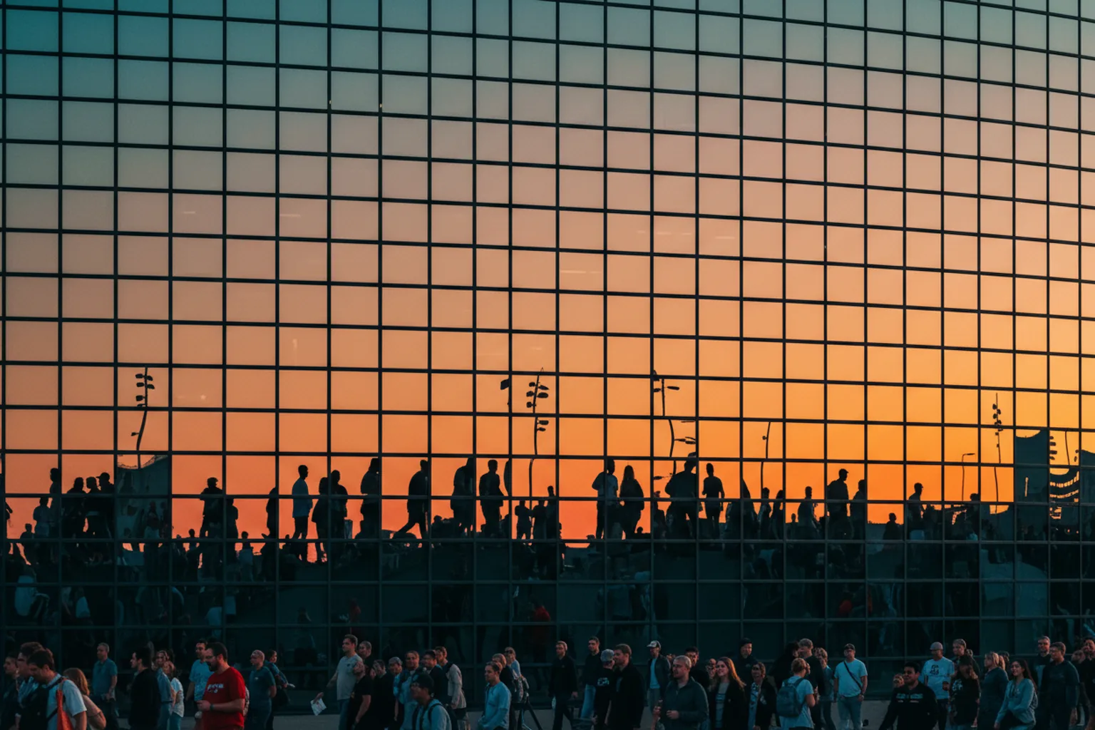 A curved glass stadium facade reflecting an aqua-and-orange sky at golden hour