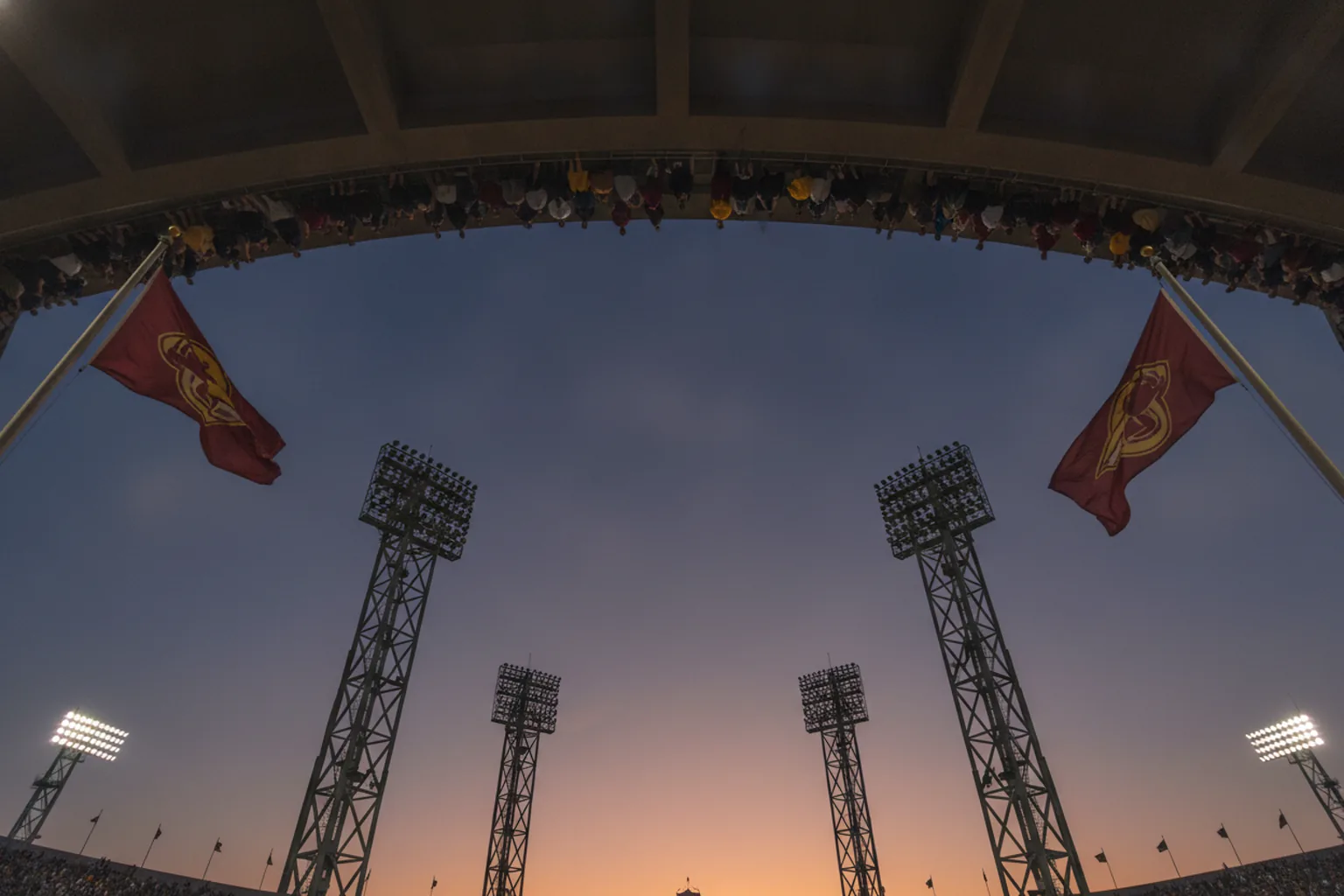 Low angle looking up at stadium floodlight pylons and pennants against a deep evening sky