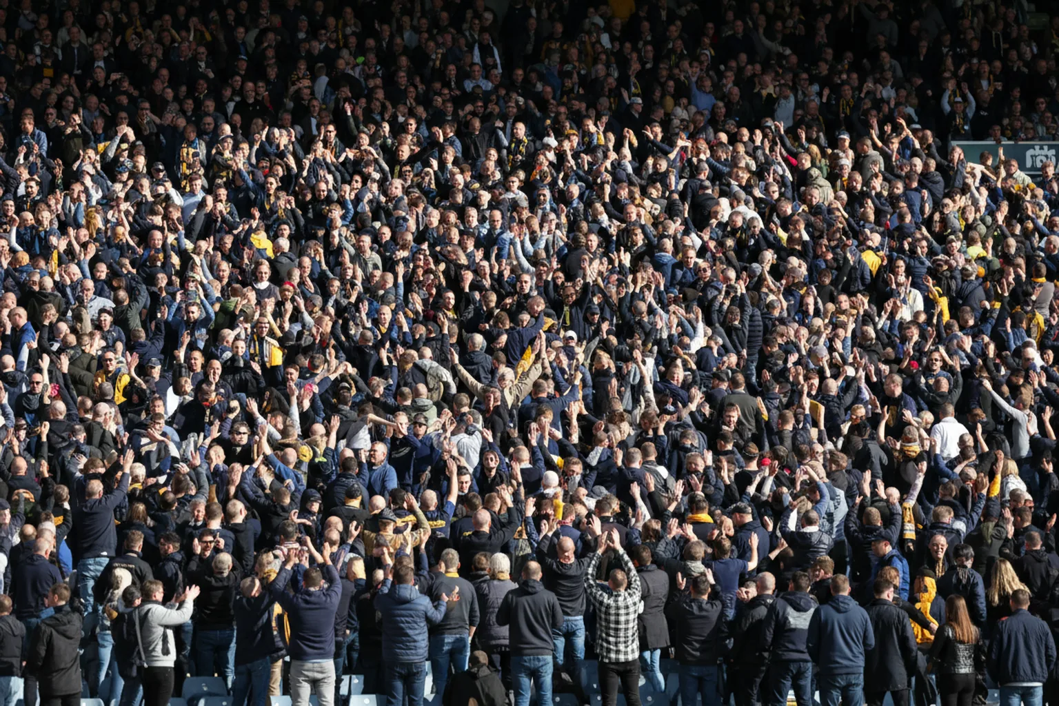 A packed section of navy-and-gold fans on their feet with arms raised in celebration