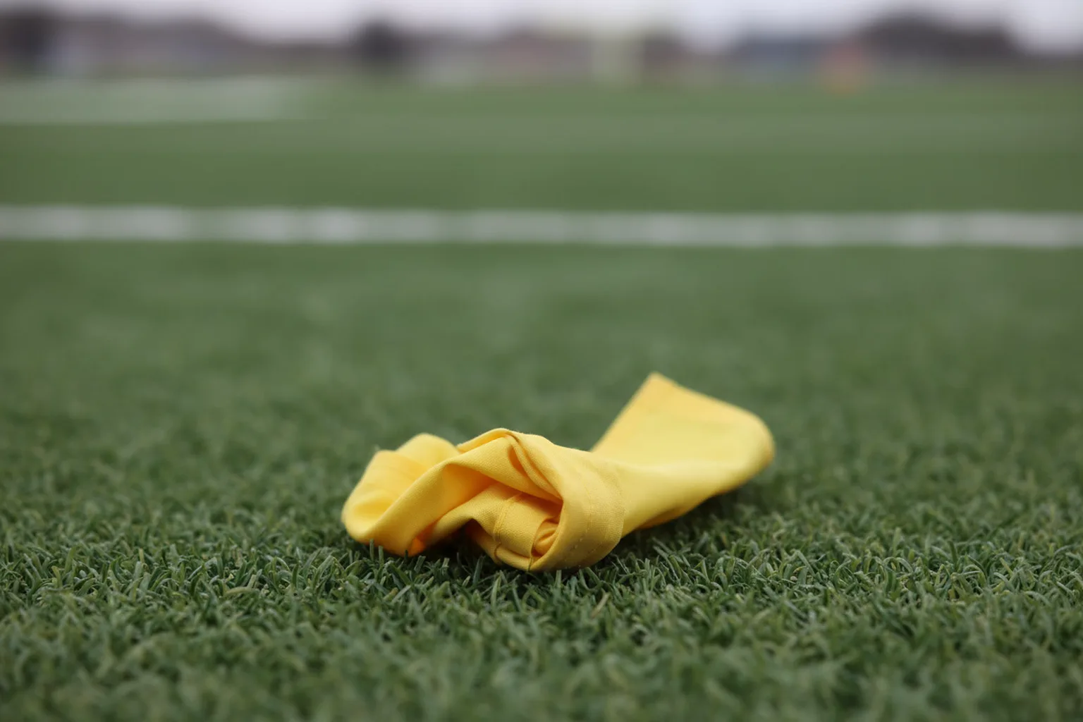 A yellow penalty flag lying on green turf in sharp focus, the field behind it thrown completely out of focus