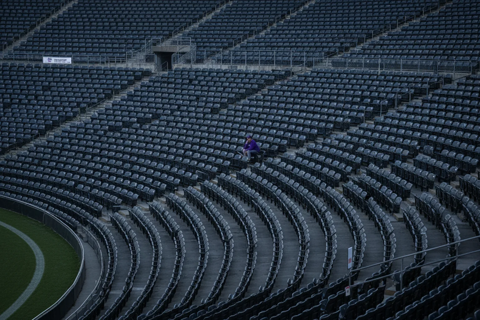 A lone fan in purple sitting by themselves high in an empty upper deck before kickoff