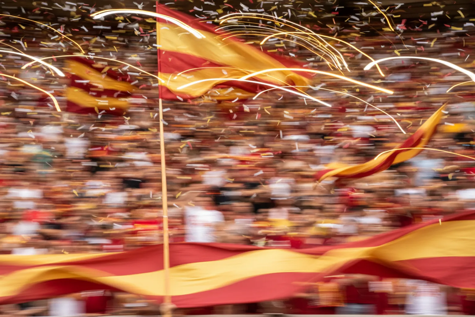 Red-and-gold team flags whipping past the camera in motion blur above a celebrating crowd